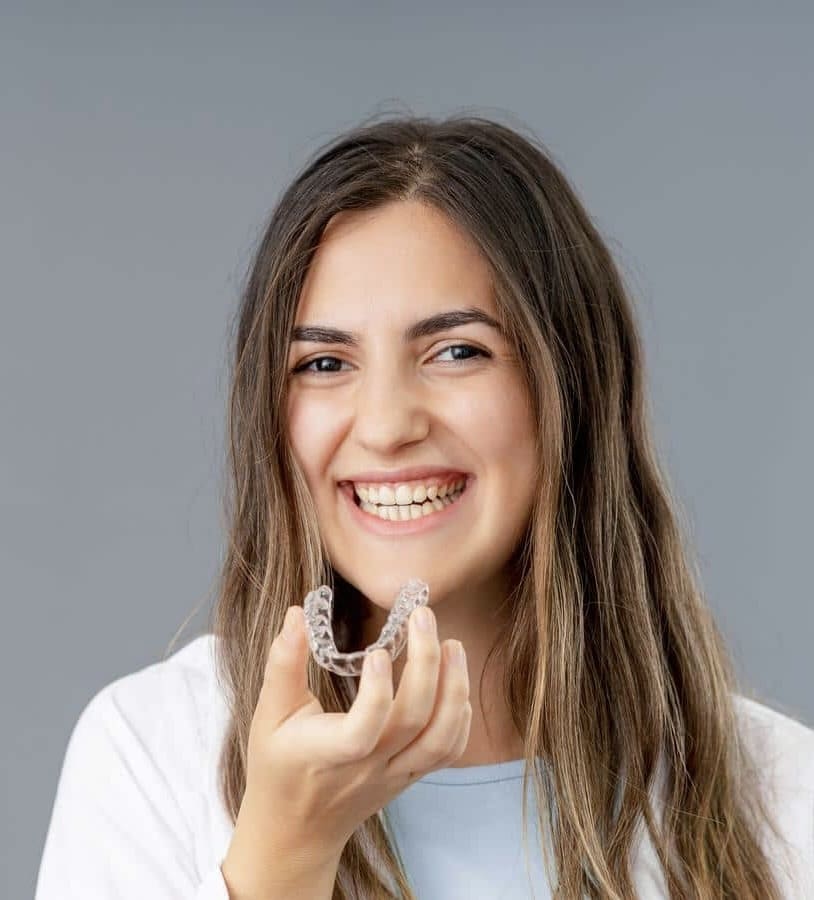 Clear-aligners-orthodontic-treatment-2 A woman smiling holding a clear plastic brace